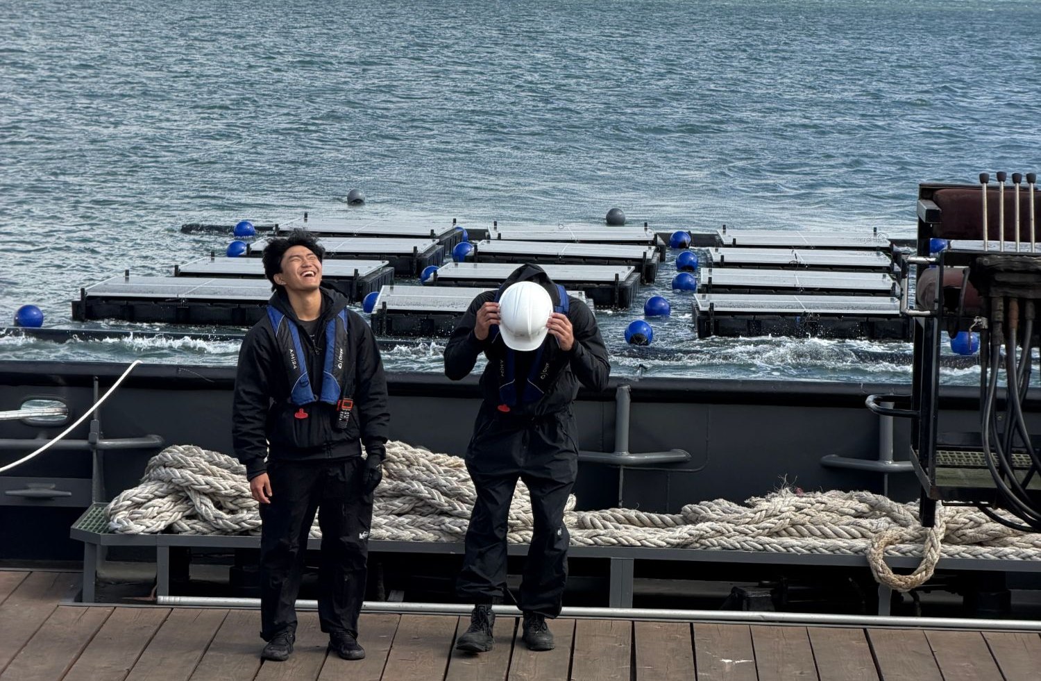 two of the team laughing on deck with the array afloat behind them